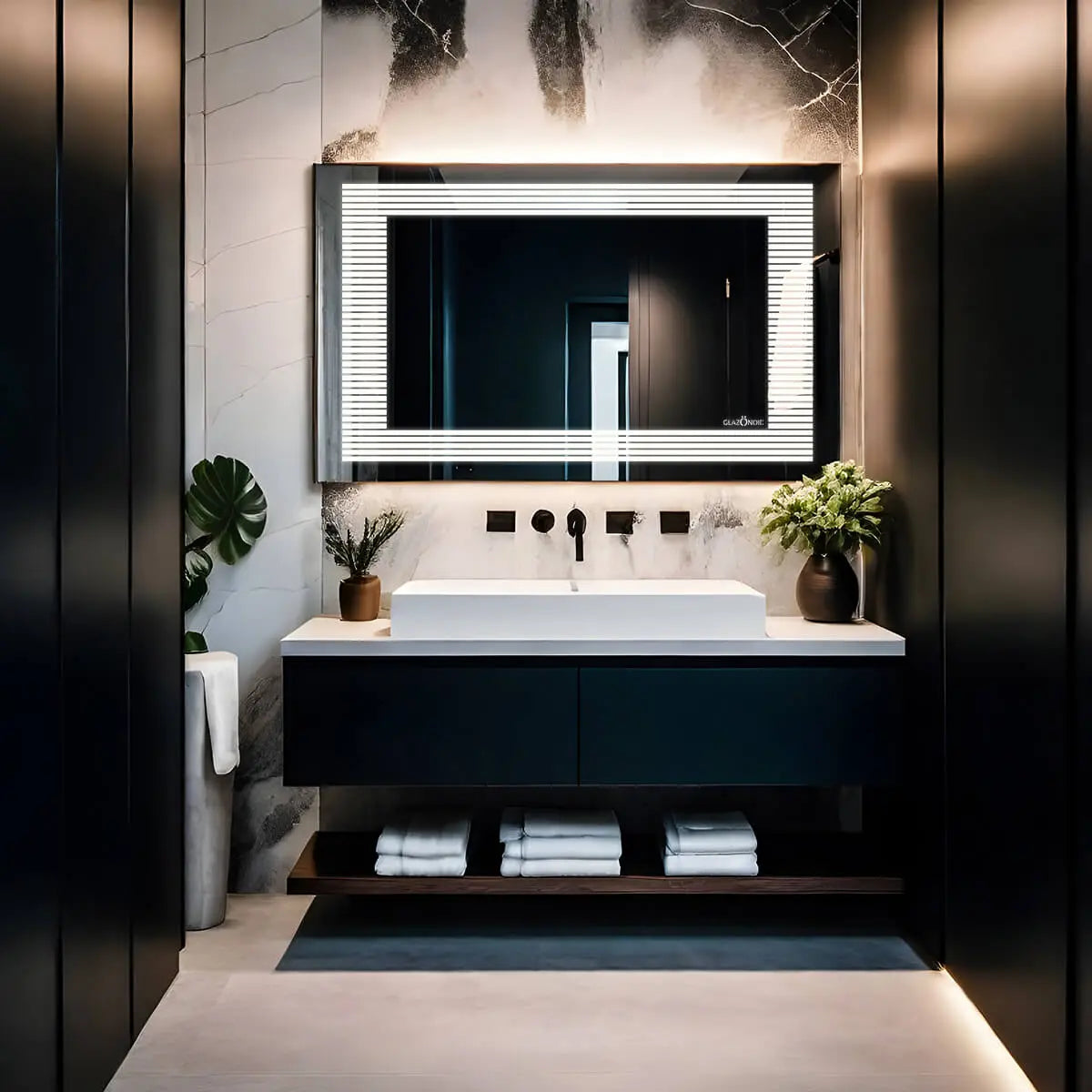 A rectangular bathroom mirror with built-in horizontal LED lights along the sides. The mirror is framed and mounted on a bathroom wall with a faucet and sink below. Text overlaid on the image reads ‘Glazonoid’