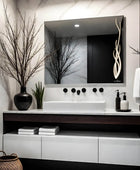 Classic white themed bathroom vanity with a rectangular LED mirror, white ceramic sink, chrome faucet, and a vase filled with pink and white flowers. A towel hanging on the wall, with 2 shampoo bottles kept on the vanity.