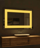A rectangular bathroom mirror with warm yellow LED backlighting on the sides. The mirror is mounted on a bathroom wall above a porcelain sink with a chrome faucet.