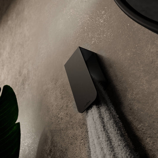 A white towel hanging on a matt black towel rack known as Aire mounted on a beige bathroom wall next to a round mirror with a black frame.