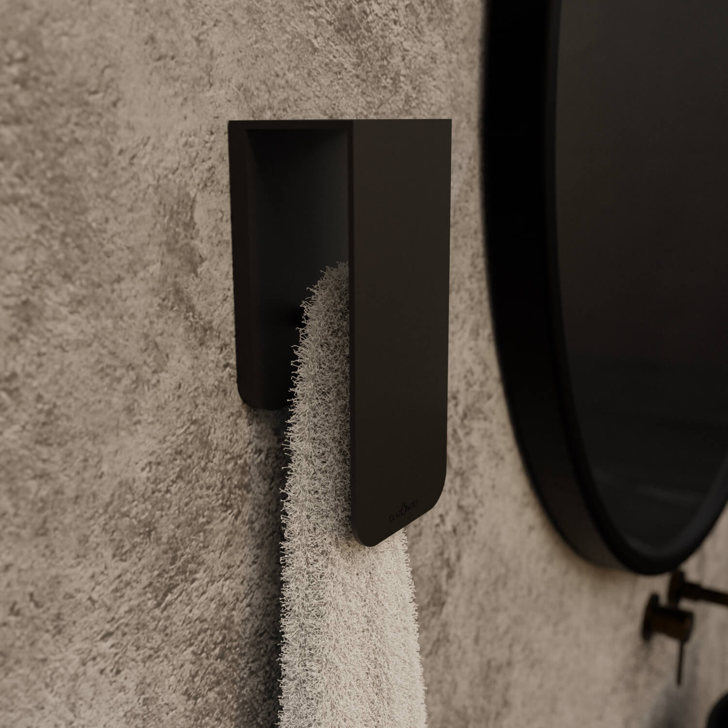 A white towel hanging on a matt black towel rack known as Aire mounted on a beige bathroom wall next to a round mirror with a black frame.