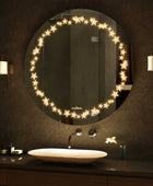 A round bathroom mirror with LED lights around the circumference. The mirror is mounted on a bathroom wall above a sink. There is text written on the bottom right corner of the mirror that says Glazonoid.