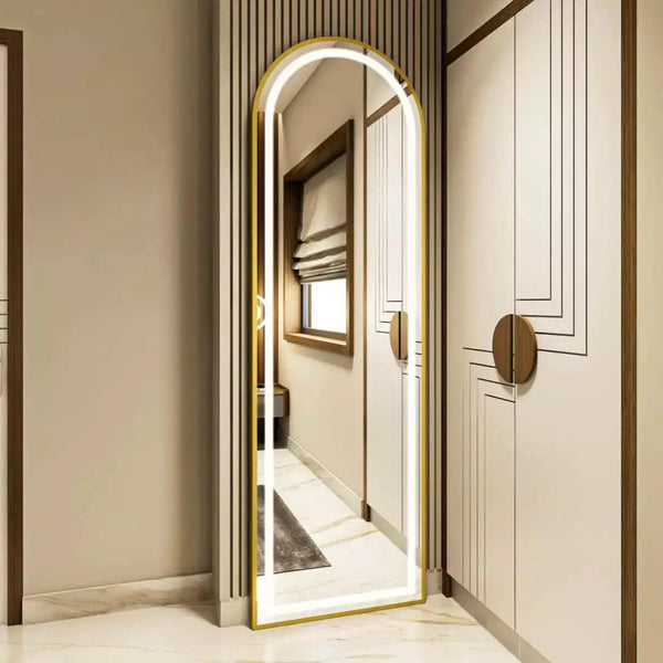 A full-length mirror with a gold frame leaning against a wall in a hallway. Next to the mirror is a white wardrobe with two doors.