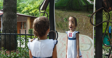 small girl standing in front curved mirror.