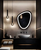 A bathroom LED mirror with a built-in digital clock icon. The time on the clock displays 11:59 PM. The LED mirror is placed on a textured wall, over a white ceramic sink and black marble vanity.