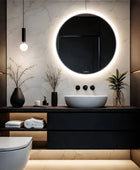 A classic bathroom with a white ceramic sink, toilet, and a round LED mirror. There is a black and white patterned shower curtain in the background. This simple and elegant bathroom design is perfect for any home. This timeless design is both stylish and functional.