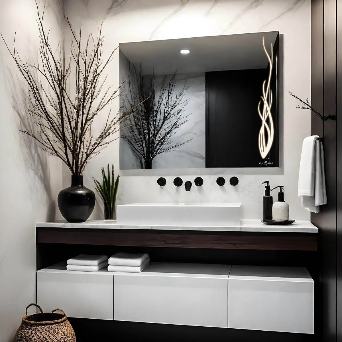 Classic white themed bathroom vanity with a rectangular LED mirror, white ceramic sink, chrome faucet, and a vase filled with pink and white flowers. A towel hanging on the wall, with 2 shampoo bottles kept on the vanity.