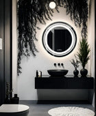 A close-up of a round bathroom LED mirror with a frameless design. The mirror is placed over the grey and black vanity which has a black ceramic sink and some plants with black pots. 