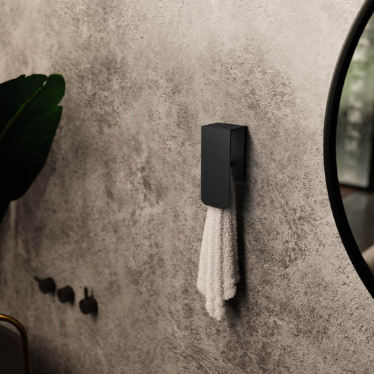 A white towel hanging on a matt black towel rack known as Aire mounted on a beige bathroom wall next to a round mirror with a black frame.