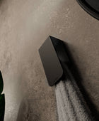 A white towel hanging on a matt black towel rack known as Aire mounted on a beige bathroom wall next to a round mirror with a black frame.