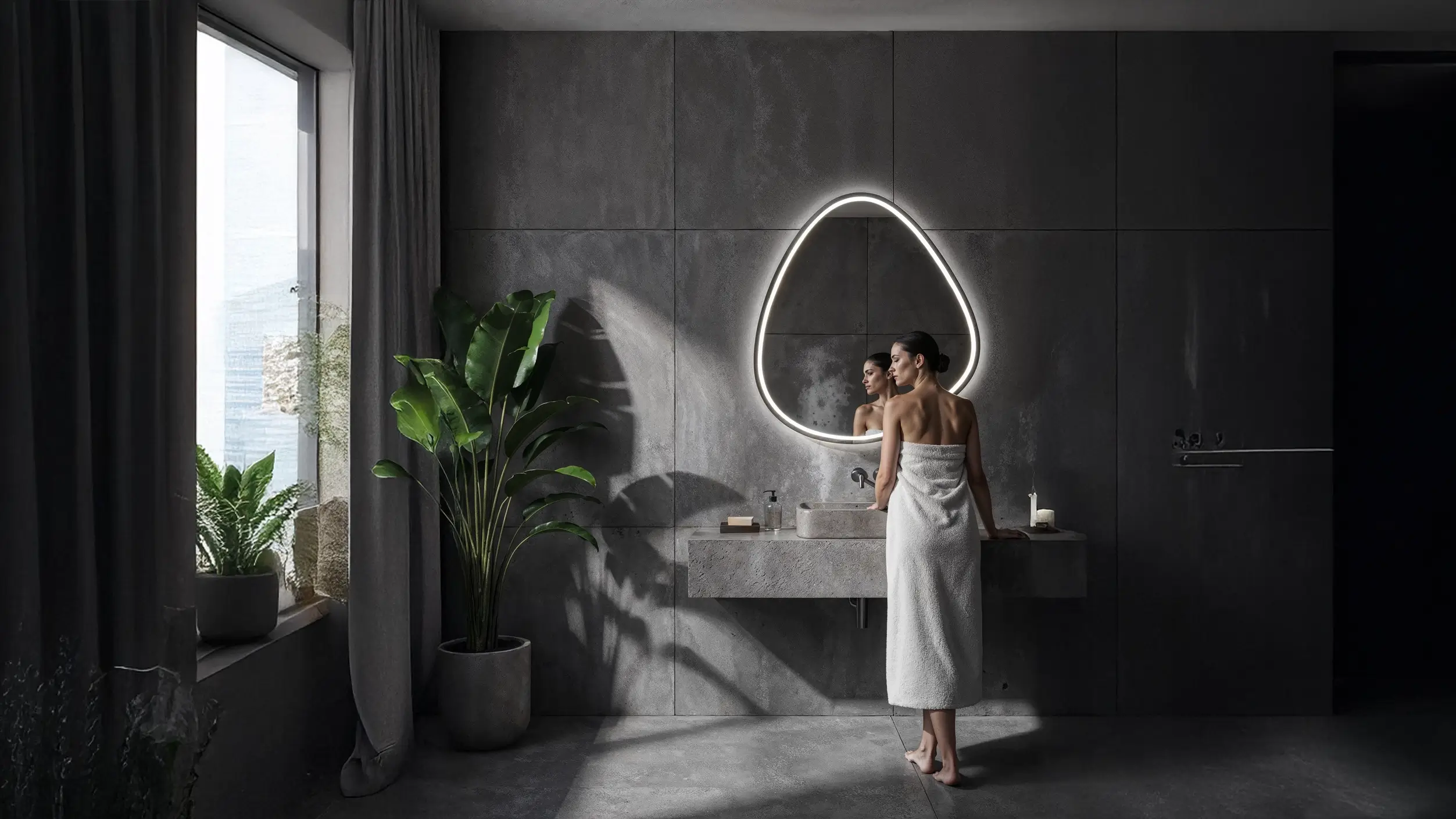 Woman standing in a modern bathroom with a large illuminated mirror.