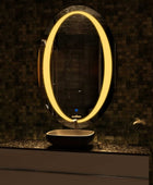 Modern bathroom mirror with a bright warm LED, in a oval shape with a chrome towel rack holding a white towel, above a white and black vanity and a black satin sink.