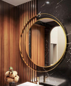 Modern and elegant bathroom vanity with a round mirror featuring a stainless steel gold colored frame and a sleek white marble sink countertop. With a plant and some perfumes kept on the counter top.